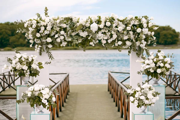 Wedding. Ceremony. Wedding arch. Wedding arch made of branches, flowers and greenery is on the green grass on the river bank