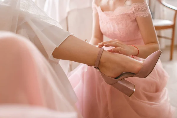 A girlfriend helps a bride to put on her wedding shoes. Beautiful female feet closeup