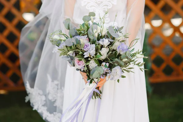 the bride on the wedding day is standing on the lawn, in the hands of a beautiful, stylish bouquet close-up