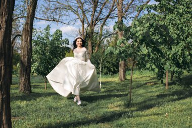 Güzel beyaz bir elbise içinde muhteşem şık siyah saçlı gelin parkta yürüyor. Kız çalışır ve saçları rüzgarda geliştirir