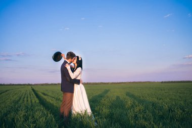 Moda gelin ve güzel gelin alan, gün batımı ve şapka elinde sarılma, adam kız öpücük