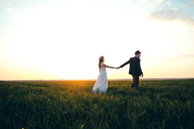 Moda koca ve güzel gelin damat şapkalı sahada, günbatımı, vardır