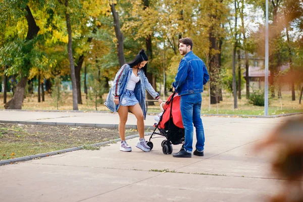 Maman et papa marchent dans le parc avec leur fille dans une poussette, une belle journée ensoleillée, une belle famille — Photo