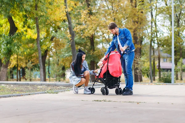 Maman et papa marchent dans le parc avec leur fille dans une poussette, une belle journée ensoleillée, une belle famille — Photo