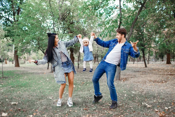 Die Familie geht im Park spazieren, die Mutter hält die kleine Tochter über dem Kopf, der Vater kümmert sich um die Familie — Stockfoto