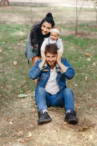 Un père heureux est assis sur une pelouse, une fille est sur ses épaules, une mère étreint une famille, une belle journée d'automne, une belle famille élégante — Photo