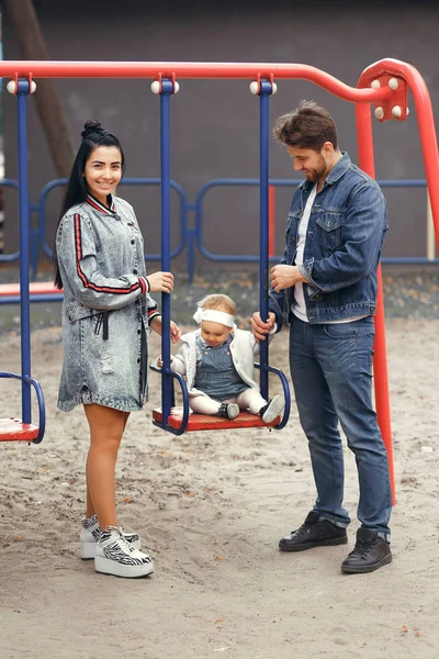 Schöne junge Eltern, spazieren gehen mit einem Kind, schaukeln es auf einer Schaukel, haben Spaß und genießen einander, glückliche Familie für einen Spaziergang — Stockfoto