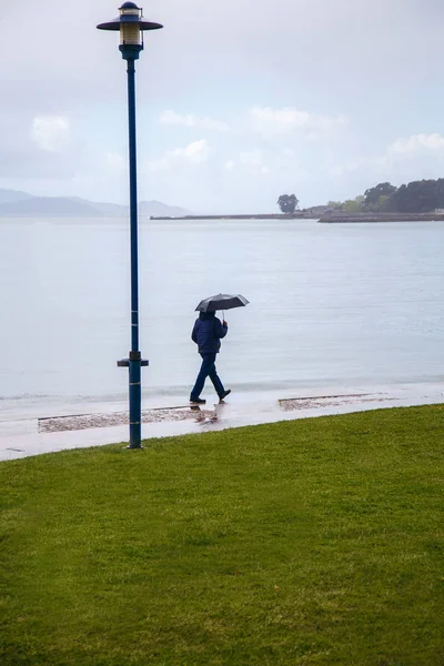 Un uomo con un ombrello sta camminando lungo l'argine, sta piovendo, l'Oceano Atlantico, maltempo — Foto Stock