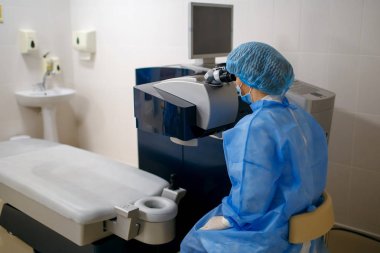 Kadın doktor işyerinde oturur ve mikroskopla bakar, bir bilim adamı çalışır, bir göz doktoru