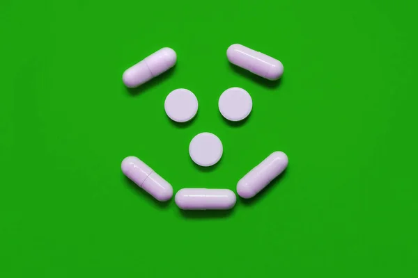 緑の背景に優しい笑顔の形で丸い楕円形の白い錠剤病気やウイルスから人を保護する医療の概念親切な医師世界的なコロナウイルスのパンデミック — ストック写真