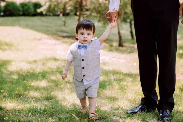 father teaches his little son to walk, family walks in the park, dad holds the child's hands and helps to walk, evening walk, father-son relationship, trust in the family, beautiful baby