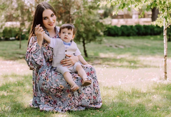 Anne ve oğlu parktaki yeşil çimlerde oturuyorlar, akşam yürüyüşü, şık giyinmiş güzel bir aile, babalarını bekliyorlar, aile değerlerini.