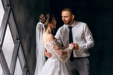 Gelin ve damat pencerede sarılıyor, erkek kızın gözlerine bakıyor ve elini tutuyor, düğün günü, aşk atmosferi, gala günü, düğün töreni.