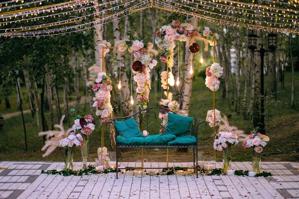 beautiful decor of fresh flowers, feathers and garlands, party lights, decorative bench, beautiful place in the park, ready for the bride and groom, wedding ceremony, place for text, candles