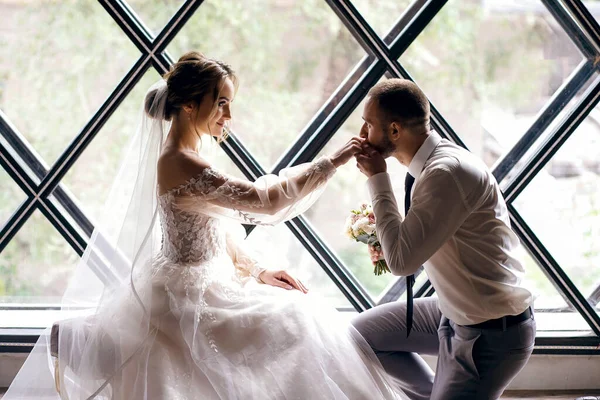 婚礼当天 一位英俊的新郎双膝跪在设计师的窗前吻着妻子的手 一个男人热情地看着他的女人的眼睛 婚礼仪式 横向的照片 — 图库照片