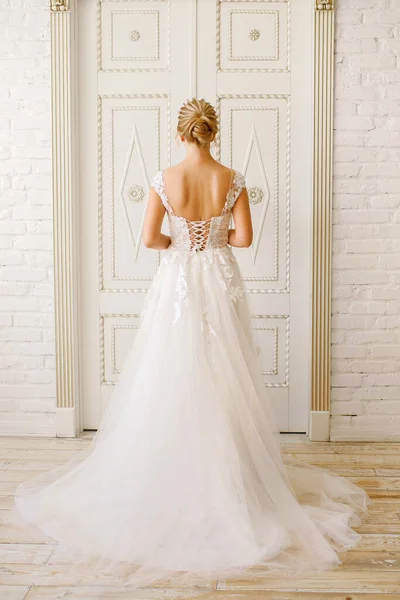 wedding day, the bride in a white long dress stands near a large wooden door, vertical picture, a blonde girl with a beautiful braided hairdo