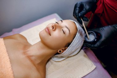 Yüz maskesi soymak, kaplıca tedavisi, cilt bakımı. Güzellik salonunda güzellik tedavisi gören bir kadın, genç bir kızın yüzüne maske takan usta bir güzellik uzmanı, mesaj için yer, yatay fotoğraf.