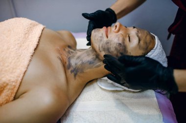 Güzel ve genç bir kadın yüz masajı, cilt bakımı, sağlık, güzellik salonunda siyah maske, mesajlaşma yeri, güzellik salonunda zevk veren bir kız, yatay bir fotoğraf.