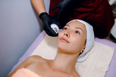 Yüz maskesi soymak, kaplıca tedavisi, cilt bakımı. Genç ve güzel bir kadın spa salonunda kozmetik ameliyatlar yaptırıyor. Güzellik uzmanı, genç bir kızın yüzüne mesaj atmak için maske takıyor.