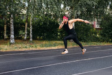 Hızlı koşucu koşarken zıplar. Siyah bir koşu bandında bir adam atletizmle meşgul. Sporcu için özel kaplamalı spor sahası, hızlı koşu, yaşam tarzı olarak spor, metin için alan