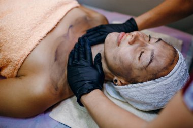 Güzel ve genç bir kadın yüz masajı, cilt bakımı, sağlık, güzellik merkezinde siyah maske, yazı için yer, güzellik salonunda işlem yapan kız, yatay fotoğraf, vücut bakımı.