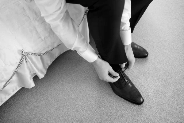 A man dresses, ties his shoes in a hotel room, the groom prepares to meet with the bride, black and white photo, focus on details, free space for text, top view, elegant guy