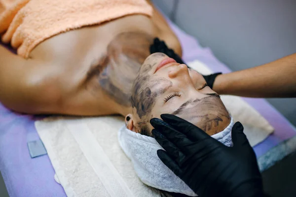 Jovem Morena Relaxante Massagem Facial Cuidados Com Pele Máscara Preta — Fotografia de Stock