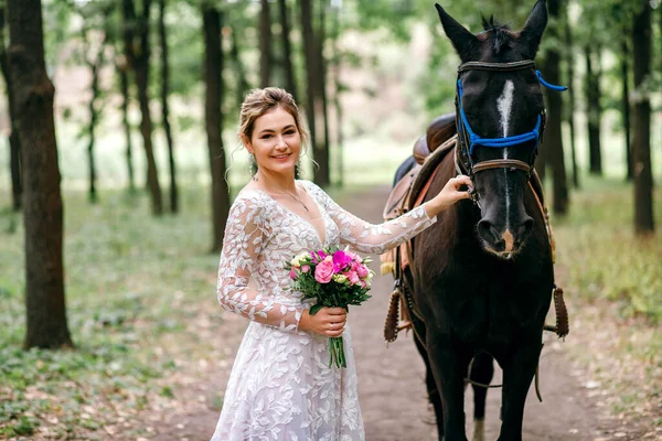 Beyaz gelinlikli güzel gelin bir atı okşuyor, siyah aygırlı bir sarışının portresi, düğün günü damat ile buluşma hazırlığı, mesajlaşma yeri, kırsal düğün konsepti.