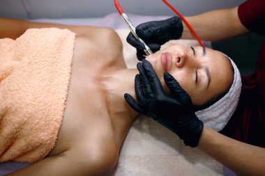 Profesyonel bir kadın kozmetik uzmanı kozmetoloji kliniğinde hidrakiyal prosedür uyguluyor. Doktor bir süpürge ile yüzün gözeneklerini temizler. Kaplıcada gençleştirme ve su kaybı