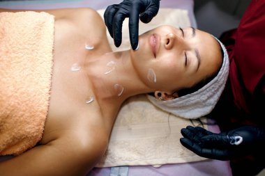 Güzeller güzeli bir esmer kaplıcada ameliyat oluyor. Güzellik uzmanı yüzüne nemlendirici sürüyor. Yüz bakımı konsepti, profesyonel kaldırma, metin için boş alan