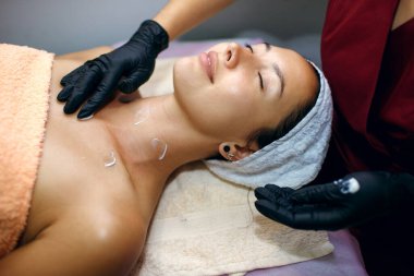 Güzel bir esmer kaplıcada tedavi görüyor, usta bir güzellik uzmanı yüzüne nemlendirici sürüyor. Yüz bakımı konsepti, profesyonel kaldırma