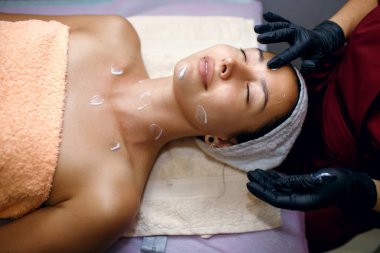 Güzeller güzeli bir esmer kaplıcada ameliyat oluyor. Güzellik uzmanı yüzüne nemlendirici sürüyor. Yüz bakımı konsepti, profesyonel kaldırma, metin için boş alan