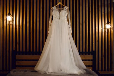 Yatağın üzerinde beyaz bir gelinlik asılı. Gelinin otel odasında geçirdiği sabah. Gelin için güzel beyaz gelinlik yatak odasında.