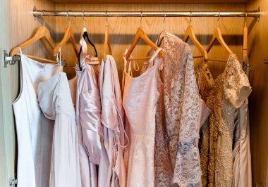 Zarif pastel pembe elbiseler dolaptaki ahşap askılarda asılı. Dolapta şenlikli saten ve dantel elbiseler var. Hassas kumaşlar, yumuşak tonlar ve elbiselerin zarif ayrıntıları kadınsı bir görünüm yaratır.