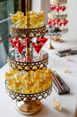 Altın katlı bir stantta zarif bardaklarda servis edilen katmanlı jöle ve kremayla gösterişli bir tatlı sergisi. Düğünler, kutlamalar ve lüks etkinlikler için mükemmel. Misafirler için tatlı ikram.