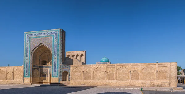 Buhara, Özbekistan 'daki Kalyan camii büyük bir panorama. Po-I-Kalyan grubundaki cami manzarası. Güneşli bir günde Orta Asya 'da antik bir bina. Bahçesinde bir ağaç olan açık kapı manzarası.