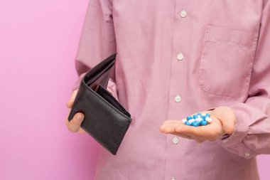 Adam boş bir cüzdan ve hap gösteriyor. Pahalı haplar. Bir kriz. Pembe arkaplan