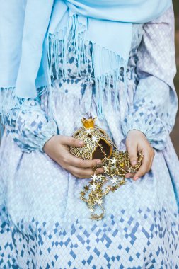 Mavi elbiseli Müslüman bir kadın ellerinde yıldızlar ve şamdanlarla bir çelenk tutuyor. Ormanın arka planına karşı.