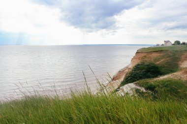 Denizin arka planında evi olan yeşil bir tepe. Yaz bulutlu günü.