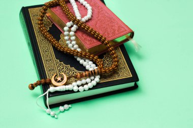 Yeşil arka planda müslüman tespihi olan iki mavi ve pembe Kuran.