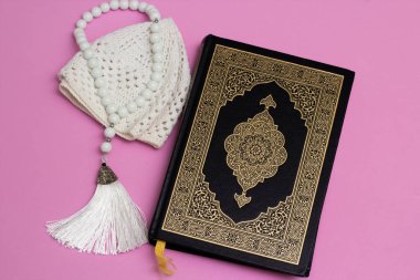 Pembe arka planda skullcap ve müslüman tespihi olan Kur 'an