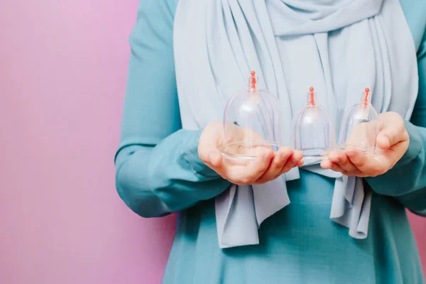 Eşarplı bir kız hijama için kavanozlarını tutuyor. Süpürge pompaları düşüyor