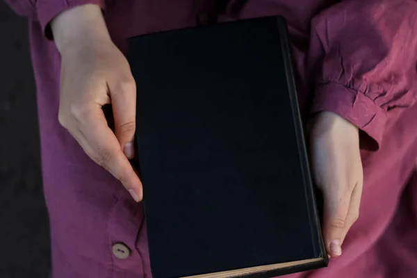 Mor elbiseli kız yerde oturuyor ve elinde siyah kapaklı bir kitap tutuyor. Şapka yakınlarda yatıyor. Kopyalama Boşluğu için Yer