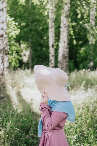 Muslim woman with a hat in a pink dress and a blue hijab with a picnic basket on a background of trees in summer. Modern muslim woman. Muslim woman in summer outfit. Ramadan.