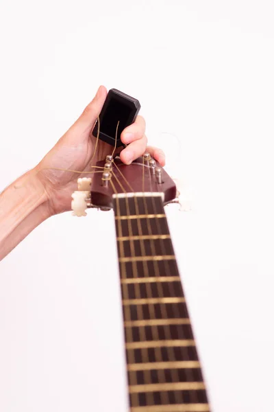 Guitar tuner. Wooden guitar on a white background. Guitar tuning. The guy tunes the guitar.