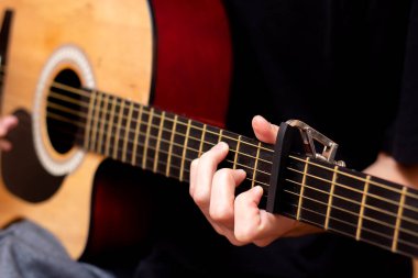 Adam gitar çalıyor. Capo gitar panosunda. Yakın plan. Tahta gitar..