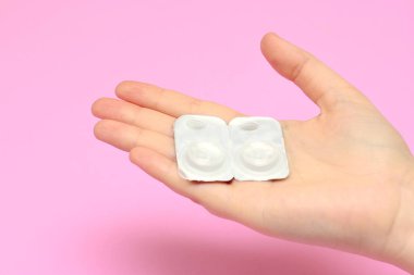 Pembe arka planda bir kadının ellerindeki ambalaj lensleri