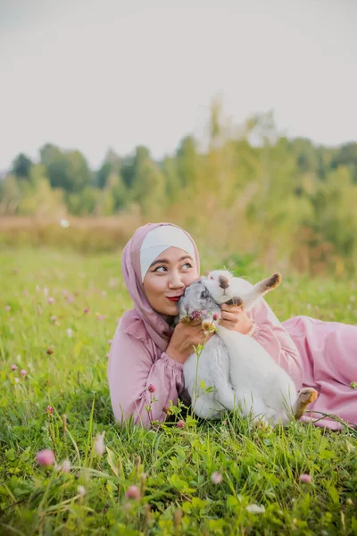 Müslüman Bir Kadın Çimenlerde Oturuyor Kollarında Iki Tavşan Tutuyor Pembe — Stok fotoğraf