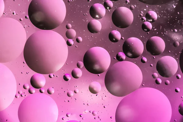 drops of oil in the form of circles and ovals chaotically located on the water surface, dark macro pink abstract background