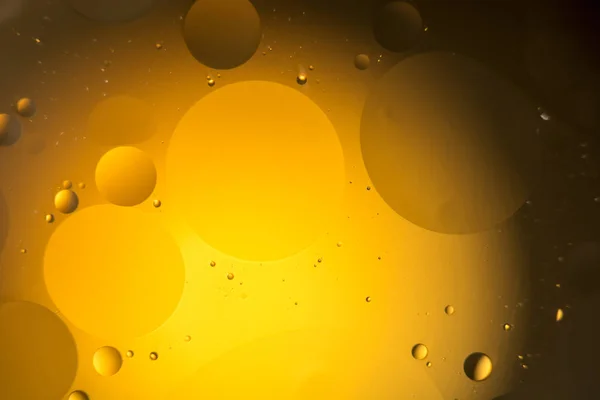 the interaction of water and oil, oil bubbles of various sizes on the water surface, yellow and black abstract macro background with soft defocusing